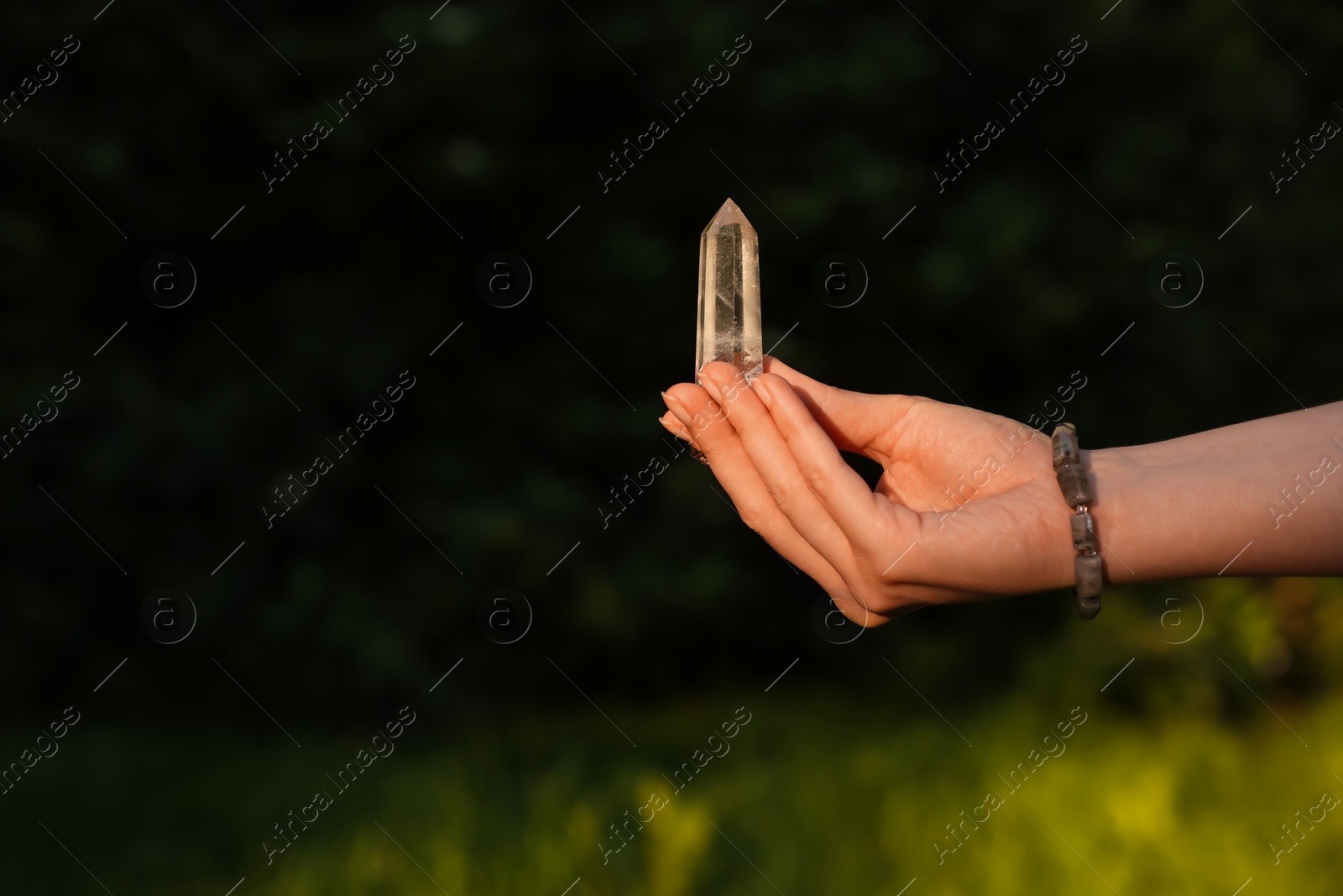Photo of Woman meditating with crystal to heal or restore her aura outdoors, closeup