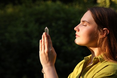 Photo of Woman meditating with crystal to heal or restore her aura outdoors