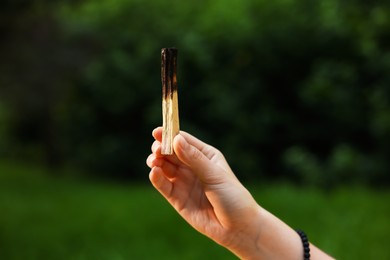 Photo of Woman meditating with Palo Santo stick to heal or restore her aura outdoors, closeup