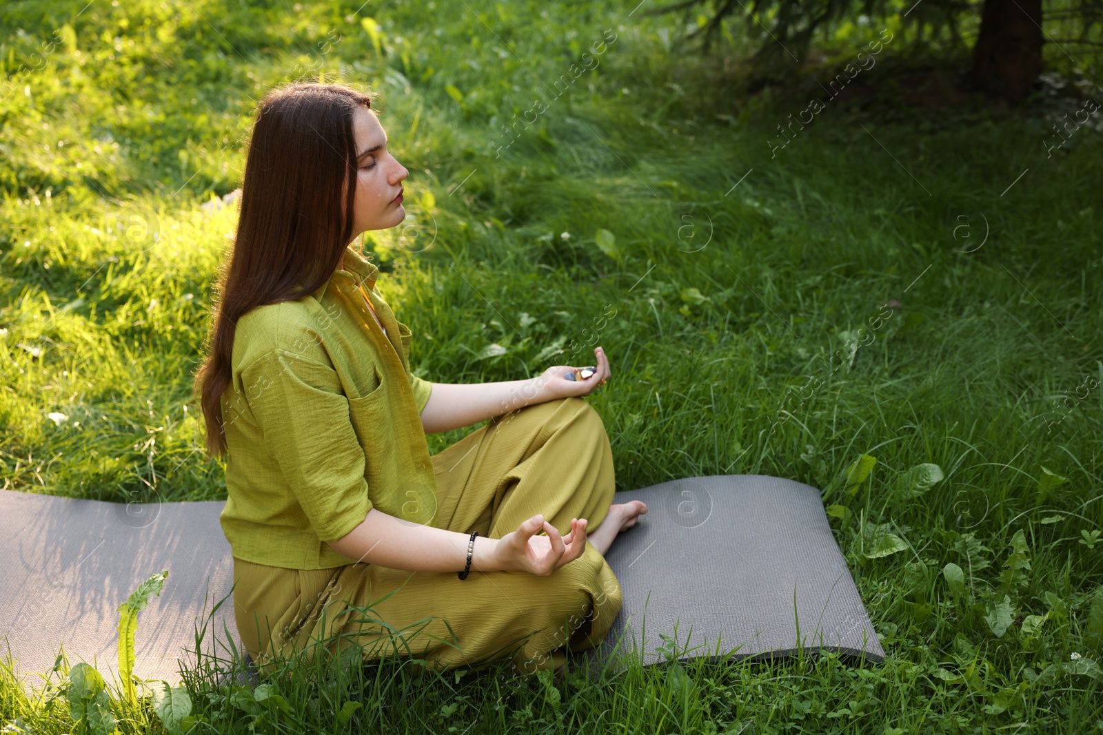 Photo of Woman meditating with crystals to heal or restore her aura outdoors, space for text