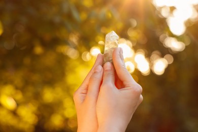 Photo of Woman meditating with crystal to heal or restore her aura outdoors, closeup