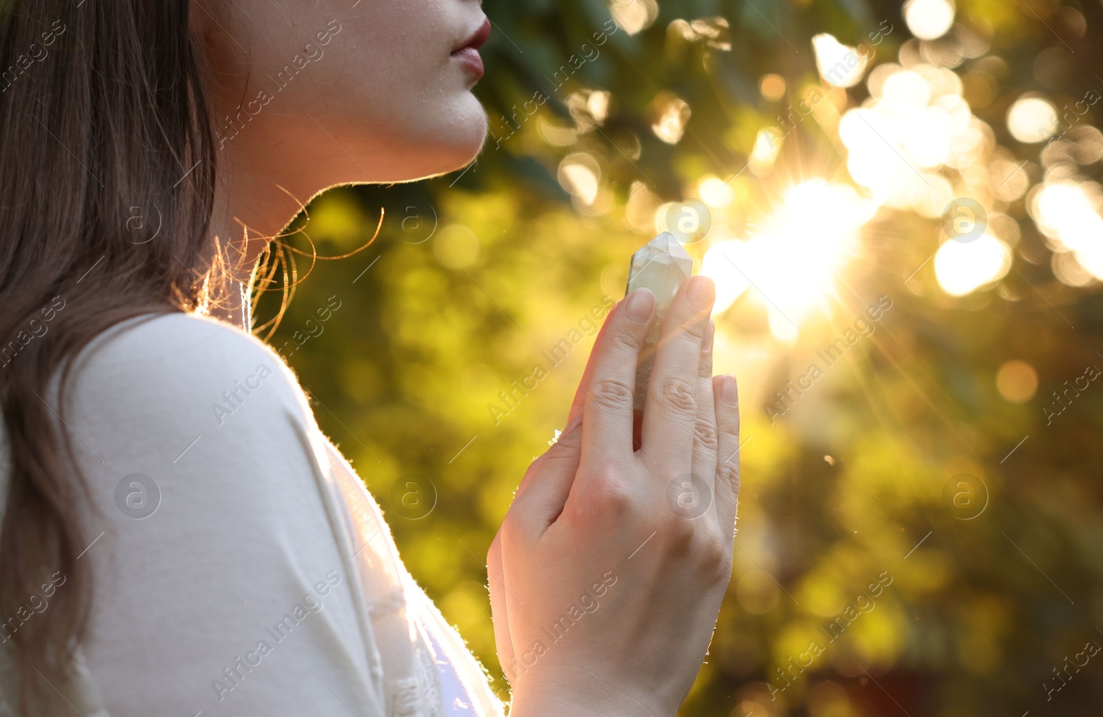 Photo of Woman meditating with crystal to heal or restore her aura outdoors, closeup