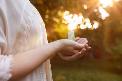 Photo of Woman meditating with crystal to heal or restore her aura outdoors, closeup