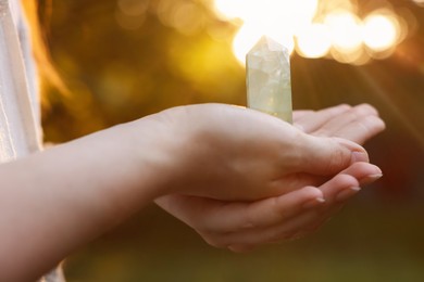 Photo of Woman meditating with crystal to heal or restore her aura outdoors, closeup