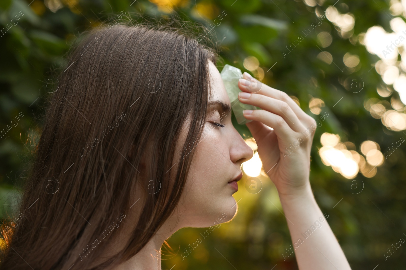 Photo of Woman meditating with crystal to heal or restore her aura outdoors