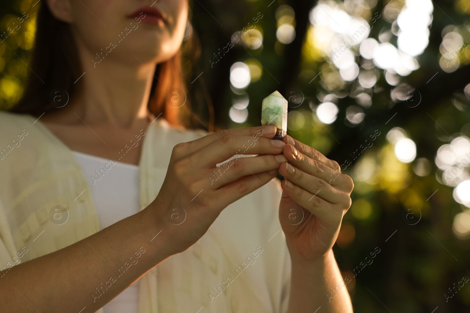 Photo of Woman meditating with crystal to heal or restore her aura outdoors, closeup