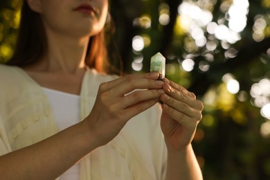 Photo of Woman meditating with crystal to heal or restore her aura outdoors, closeup