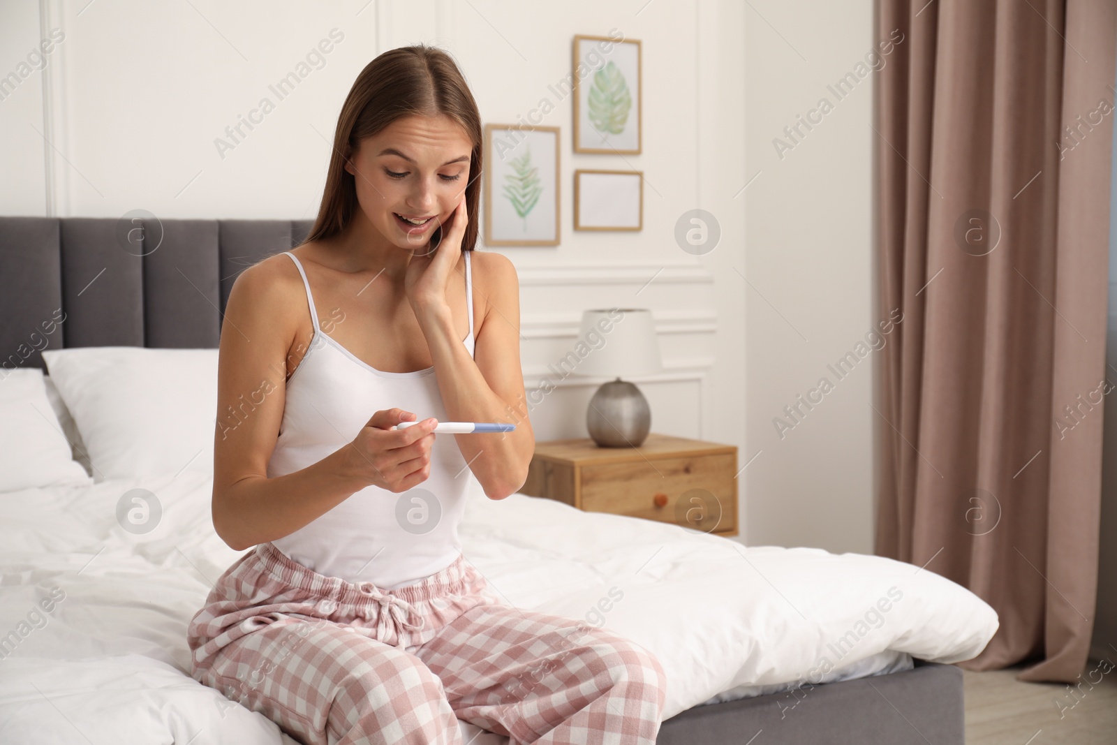 Happy young woman with pregnancy test on bed at home Photo of Happy young woman with pregnancy test on bed at home