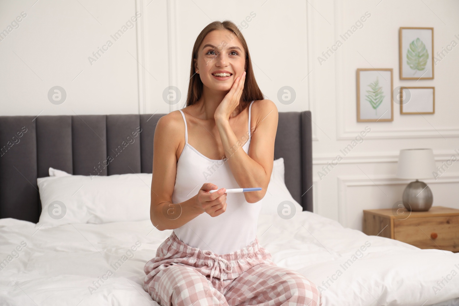 Happy young woman with pregnancy test on bed at home Photo of Happy young woman with pregnancy test on bed at home