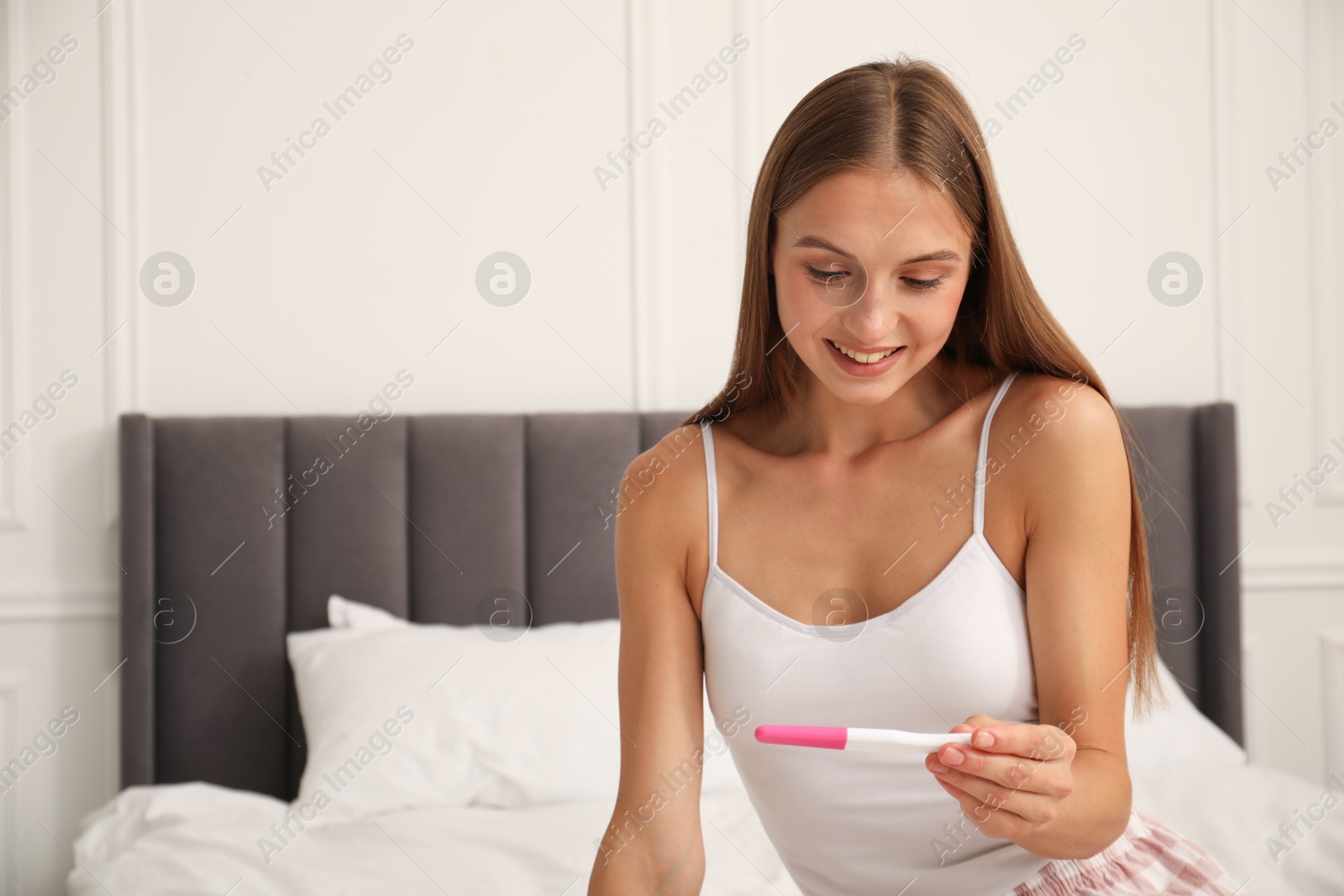 Happy young woman with pregnancy test on bed at home Photo of Happy young woman with pregnancy test on bed at home
