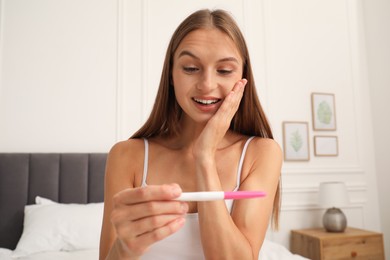 Photo of Happy young woman with pregnancy test in bedroom