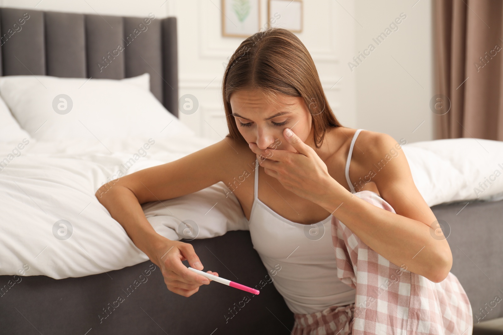 Worried young woman with pregnancy test on floor in bedroom Photo of Worried young woman with pregnancy test on floor in bedroom
