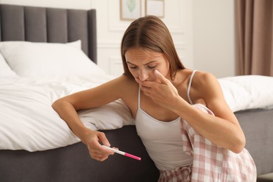 Photo of Worried young woman with pregnancy test on floor in bedroom