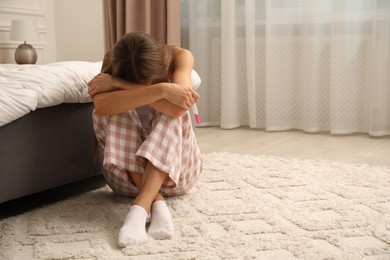 Photo of Upset woman with pregnancy test on floor in bedroom, space for text