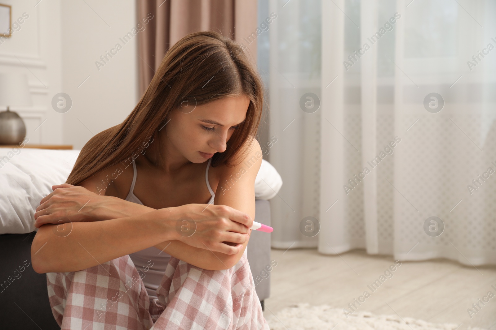 Worried young woman with pregnancy test on floor in bedroom Photo of Worried young woman with pregnancy test on floor in bedroom