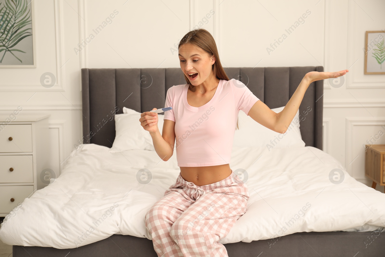 Happy young woman with pregnancy test on bed at home Photo of Happy young woman with pregnancy test on bed at home