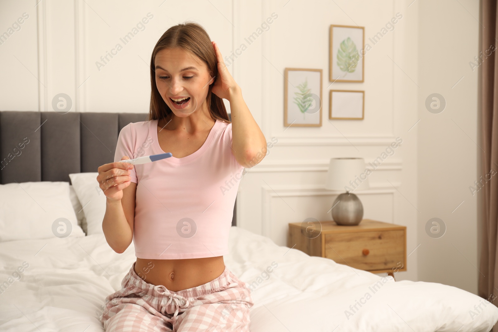 Happy young woman with pregnancy test on bed at home Photo of Happy young woman with pregnancy test on bed at home