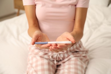 Photo of Woman with pregnancy test on bed at home, closeup