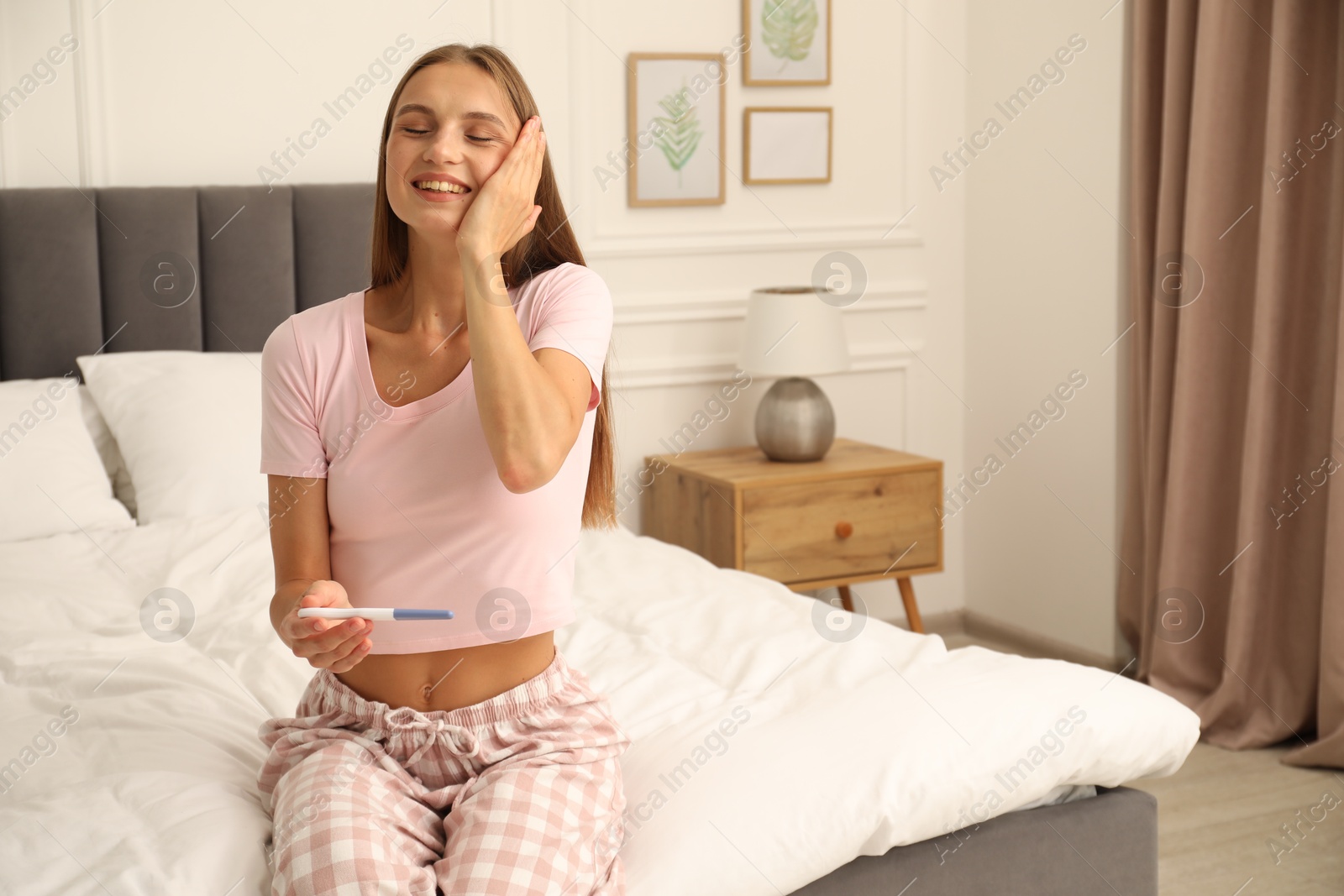 Happy young woman with pregnancy test on bed at home Photo of Happy young woman with pregnancy test on bed at home