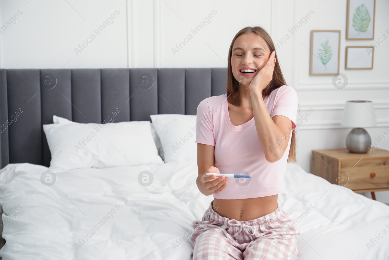 Happy young woman with pregnancy test on bed at home Photo of Happy young woman with pregnancy test on bed at home
