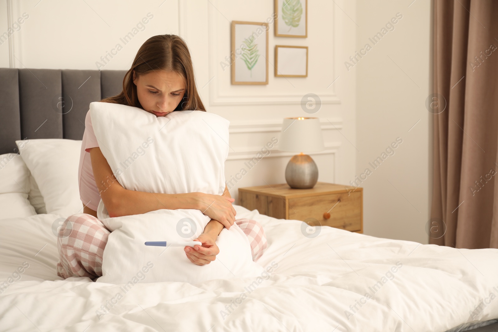 Worried young woman with pregnancy test on bed at home Photo of Worried young woman with pregnancy test on bed at home