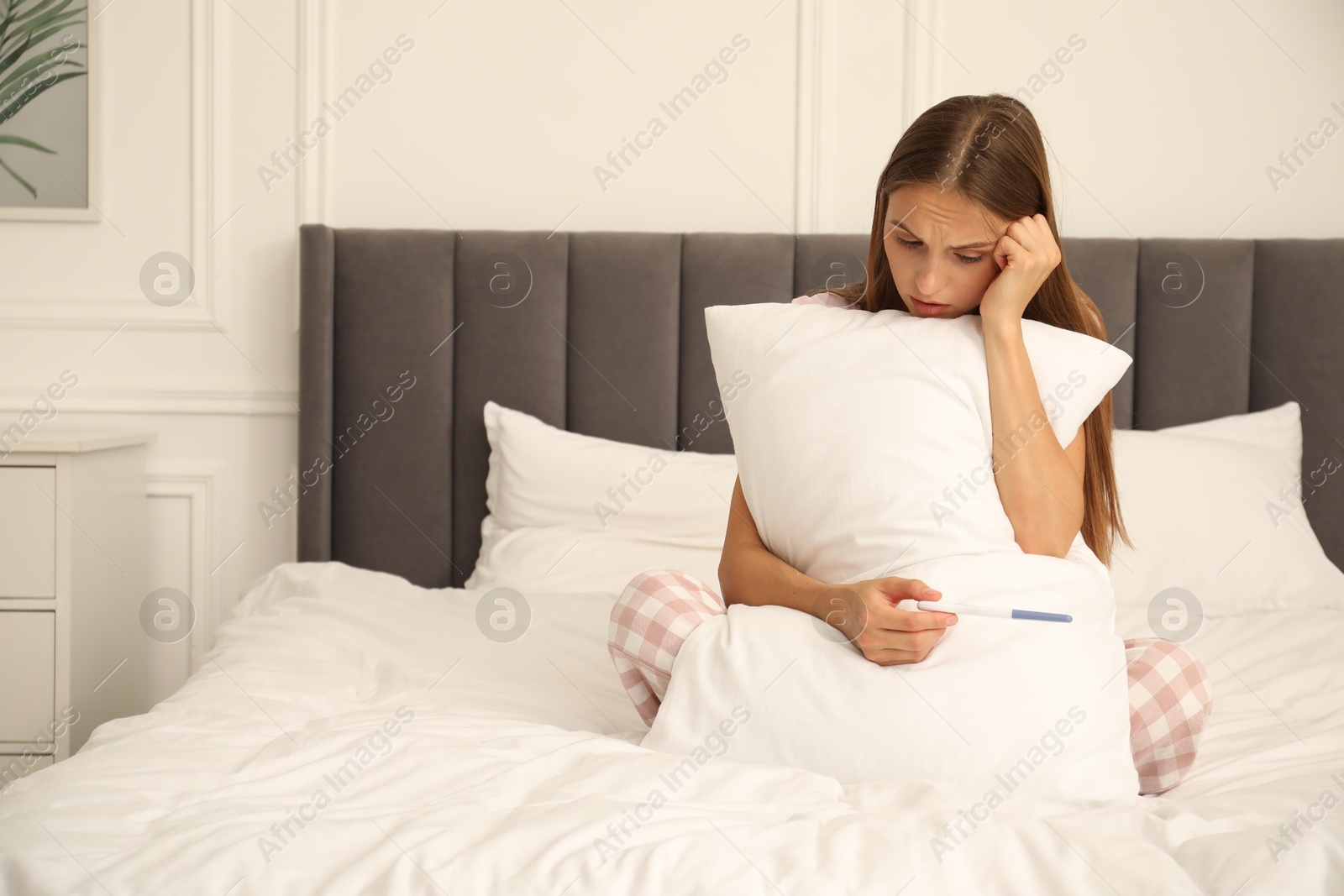 Worried young woman with pregnancy test on bed at home Photo of Worried young woman with pregnancy test on bed at home