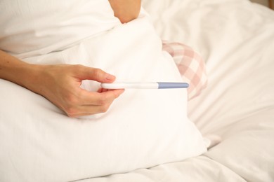 Photo of Woman with pregnancy test on bed at home, closeup