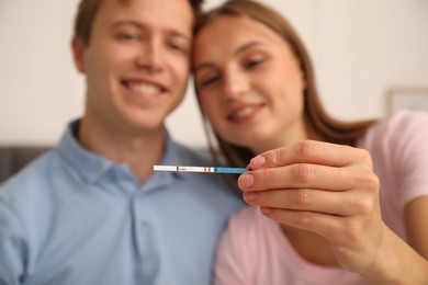 Photo of Happy couple with positive pregnancy test at home, selective focus
