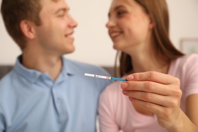 Photo of Happy couple with positive pregnancy test at home, selective focus