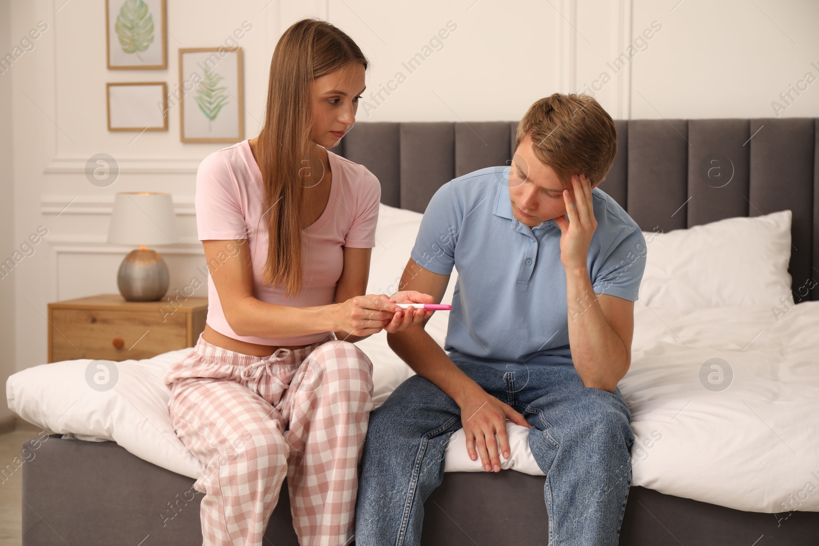 Photo of Worried couple with pregnancy test on bed at home