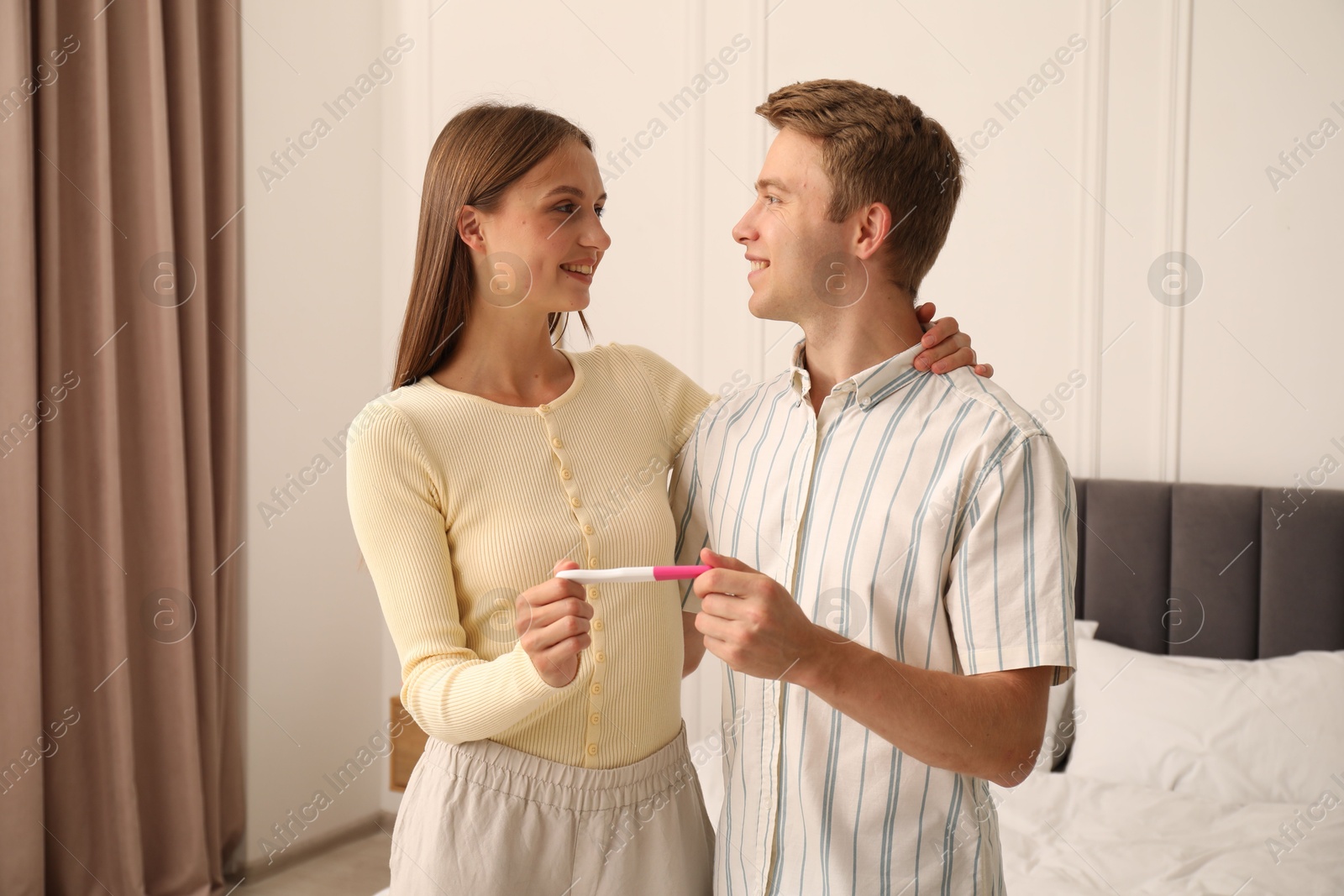 Happy couple with pregnancy test in bedroom Photo of Happy couple with pregnancy test in bedroom