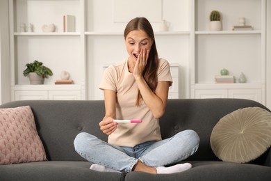 Photo of Excited young woman with pregnancy test on sofa at home