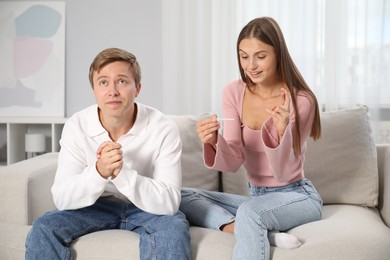Photo of Emotional couple with pregnancy test waiting for result on sofa at home