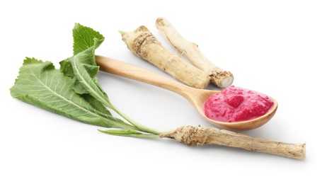 Photo of Tasty horseradish sauce with beetroot in spoon, roots and leaves isolated on white