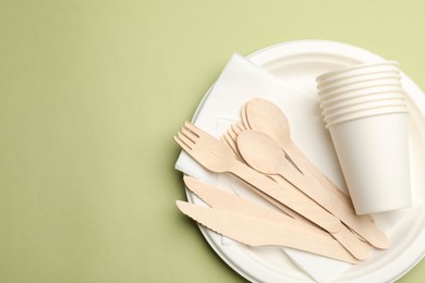 Photo of Set of disposable tableware on olive background, top view. Space for text