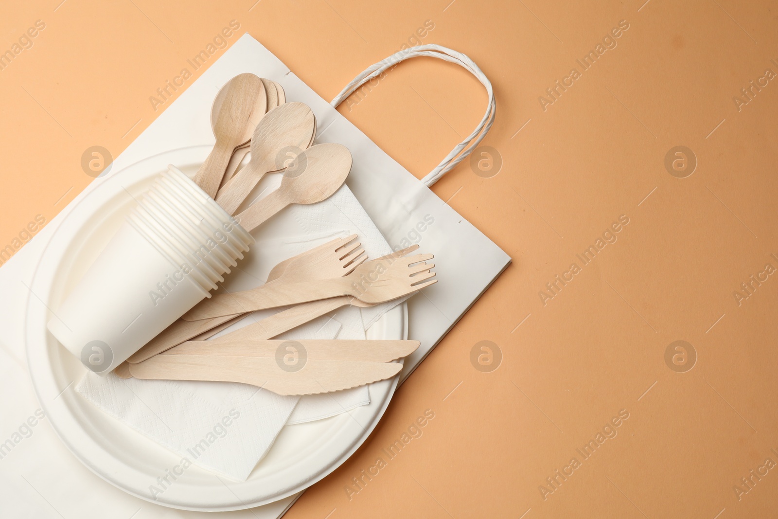 Photo of Set of disposable tableware on pale orange background, top view. Space for text