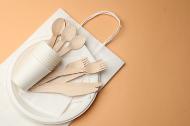 Photo of Set of disposable tableware on pale orange background, top view. Space for text