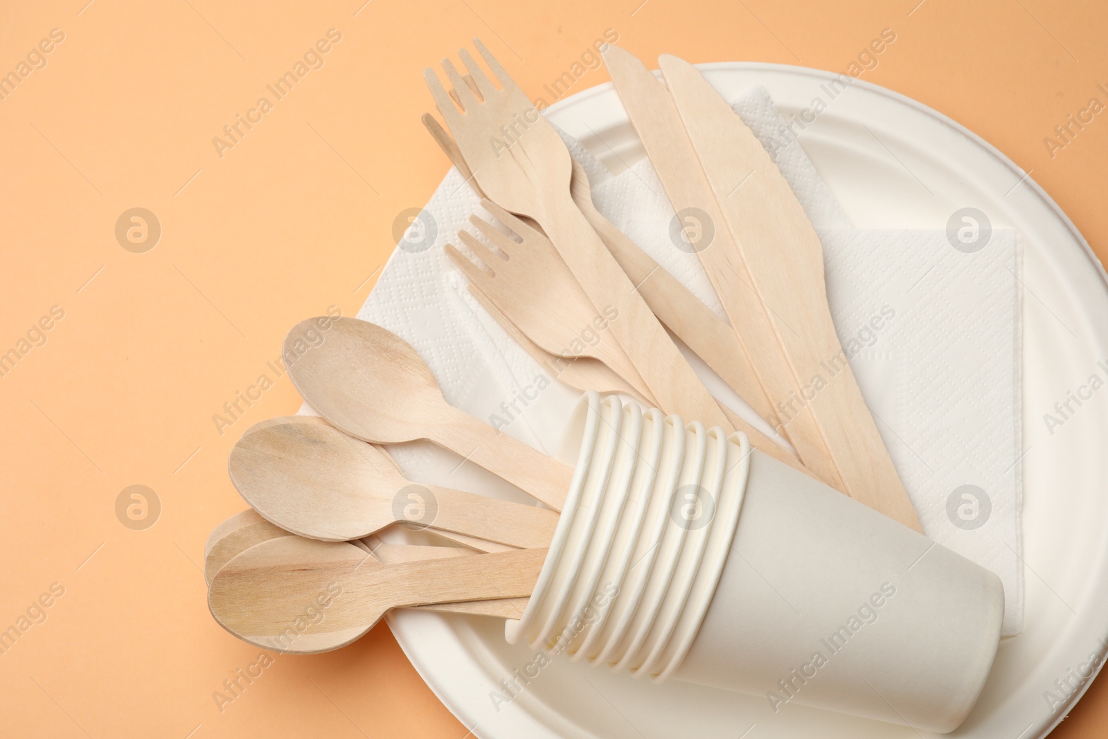 Photo of Set of disposable tableware on pale orange background, top view