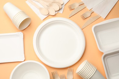 Photo of Set of disposable tableware on pale orange background, flat lay