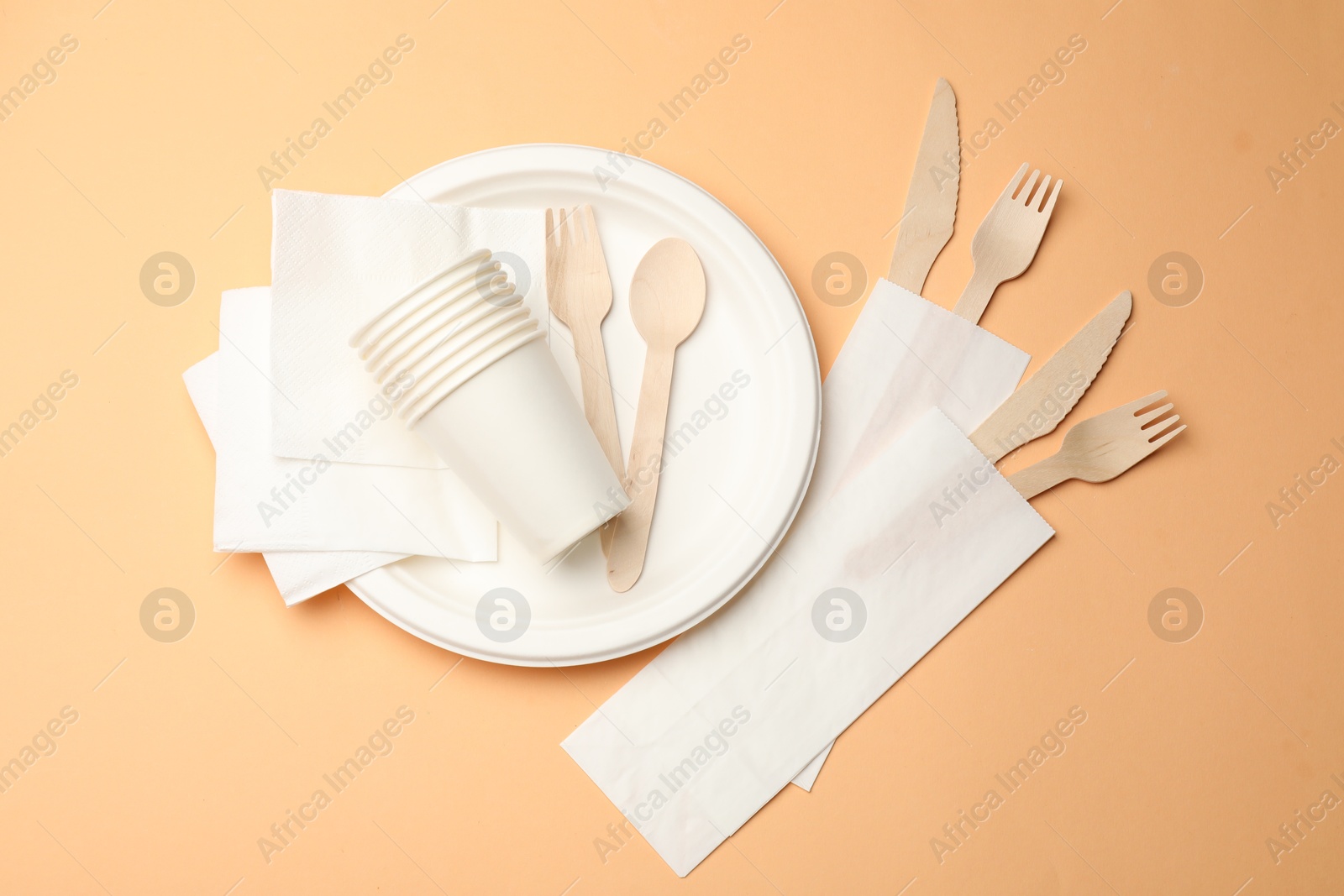 Photo of Set of disposable tableware on pale orange background, flat lay