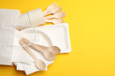Photo of Set of disposable tableware on yellow background, flat lay. Space for text