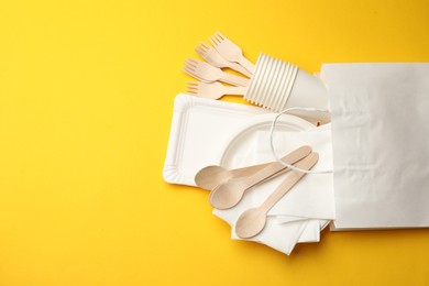 Photo of Set of disposable tableware on yellow background, flat lay. Space for text