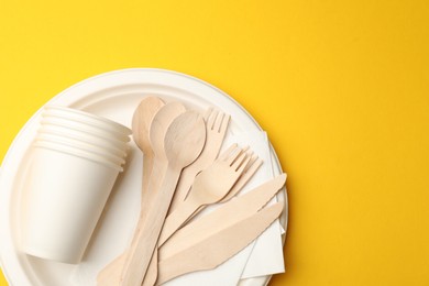 Photo of Set of disposable tableware on yellow background, top view. Space for text