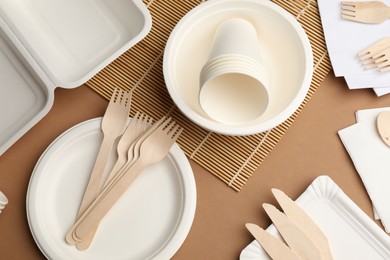 Photo of Set of disposable tableware on brown background, flat lay