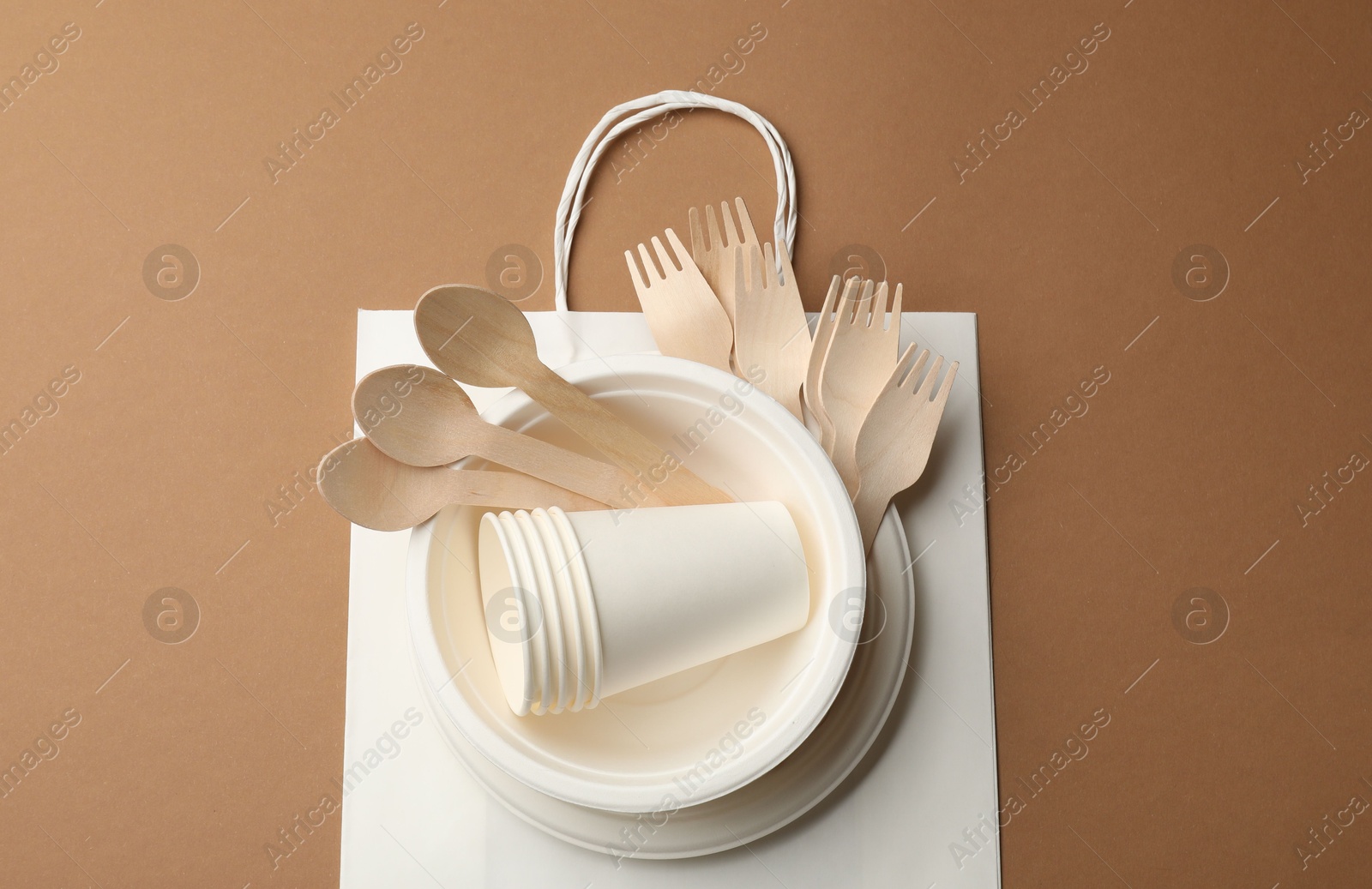 Set of disposable tableware on brown background, top view Photo of Set of disposable tableware on brown background, top view