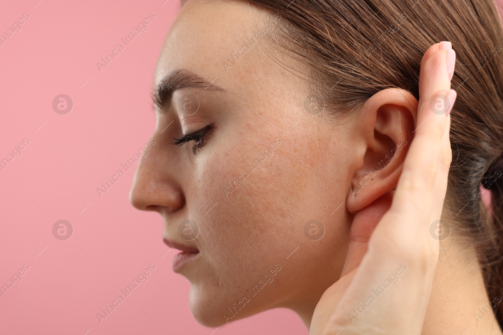 Photo of Sound. Woman showing hand to ear gesture on pink background, closeup