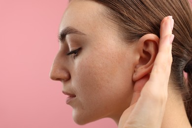 Photo of Sound. Woman showing hand to ear gesture on pink background, closeup