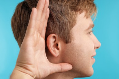 Photo of Sound. Sound. Man showing hand to ear gesture on light blue background
