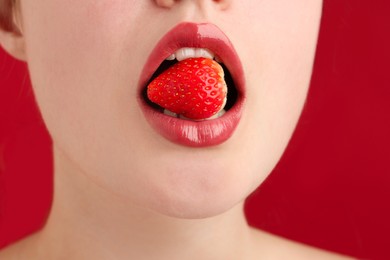 Photo of Woman with beautiful lips makeup and strawberry on red background, closeup