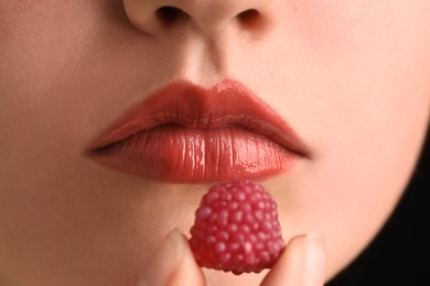 Photo of Woman with beautiful lips makeup and raspberry candy on black background, closeup